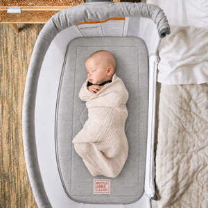 Wholesome Linen organic flax mattress for Baby Delight Beside Me Serenity bassinet, gray linen mattress with embroidered logo and sleeping baby.